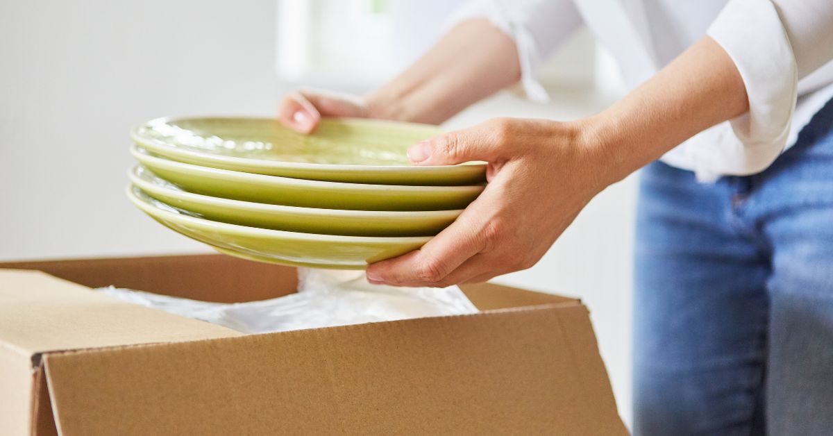 person packing green plates into a cardboard box - 247 Self Storage self storage